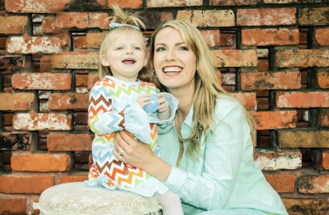 A mother and child smiling together against a brick wall